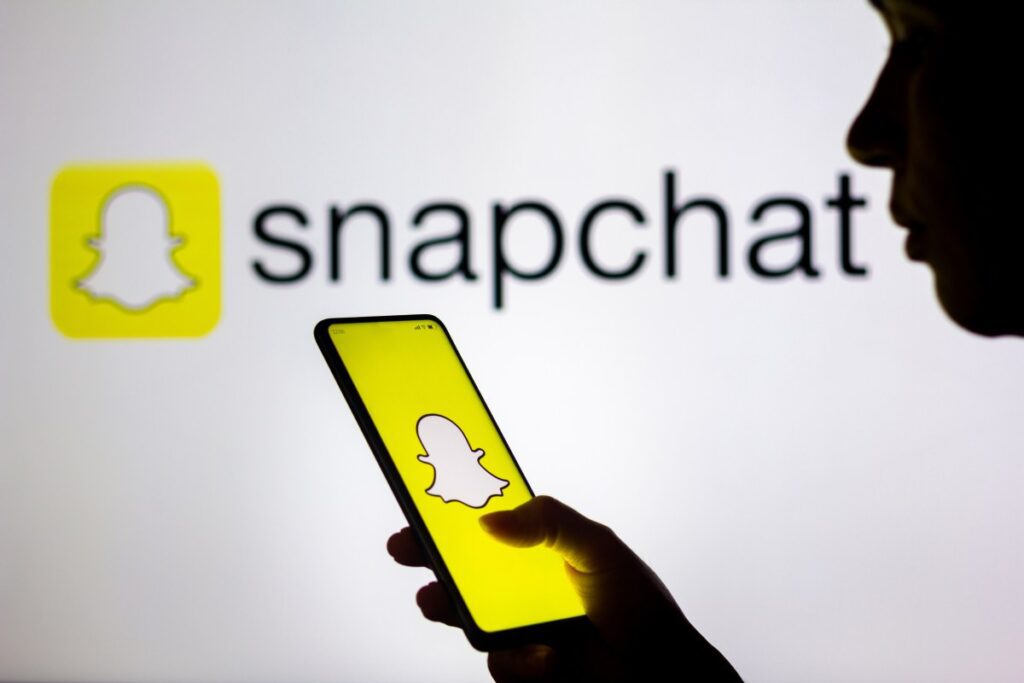 In this photo illustration, a woman's silhouette holds a smartphone with the Snapchat logo displayed on the screen and in the background.